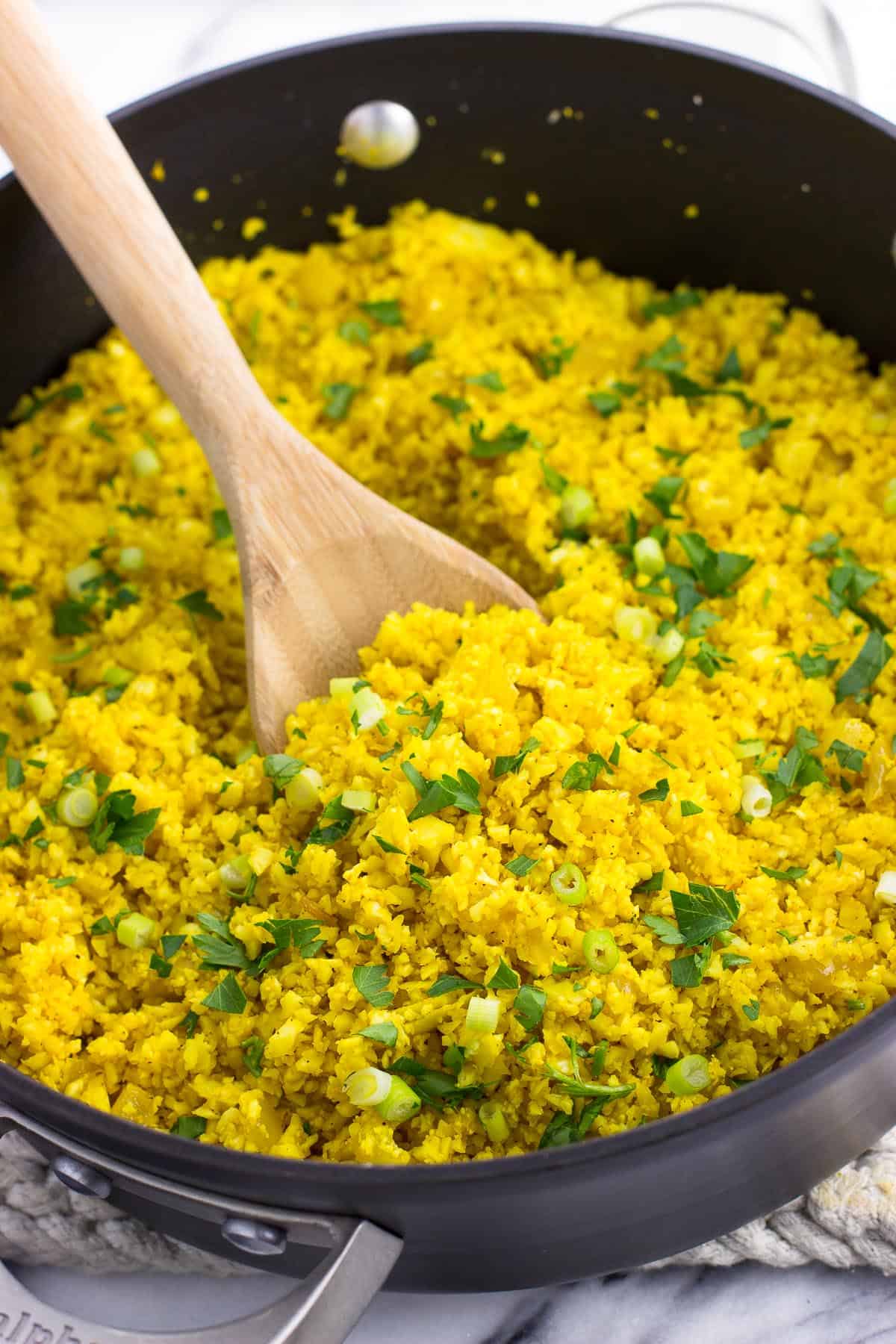 Ginger turmeric cauliflower rice in a pan garnished with greens.