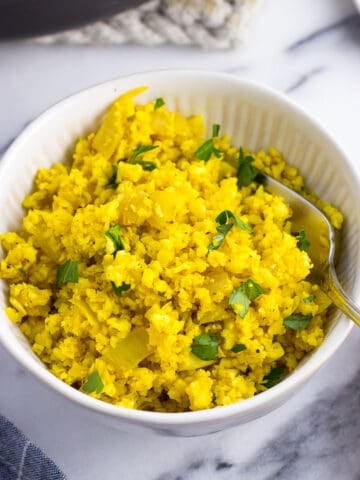 A small bowl of turmeric cauliflower rice with a fork.