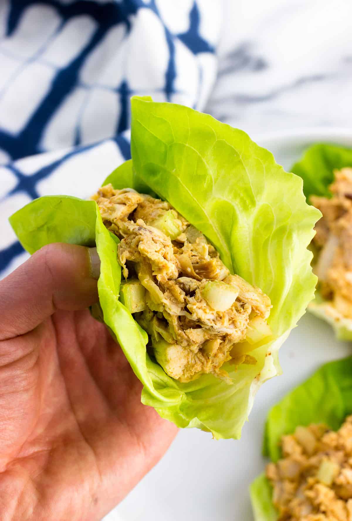 A hand holding a chicken salad lettuce wrap cup.