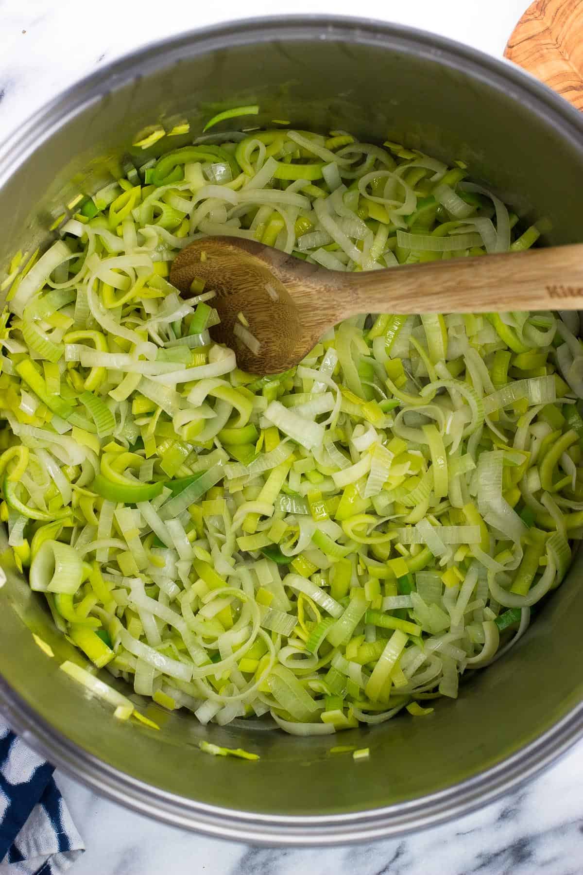 A wooden spoon in the pot of sliced leeks.