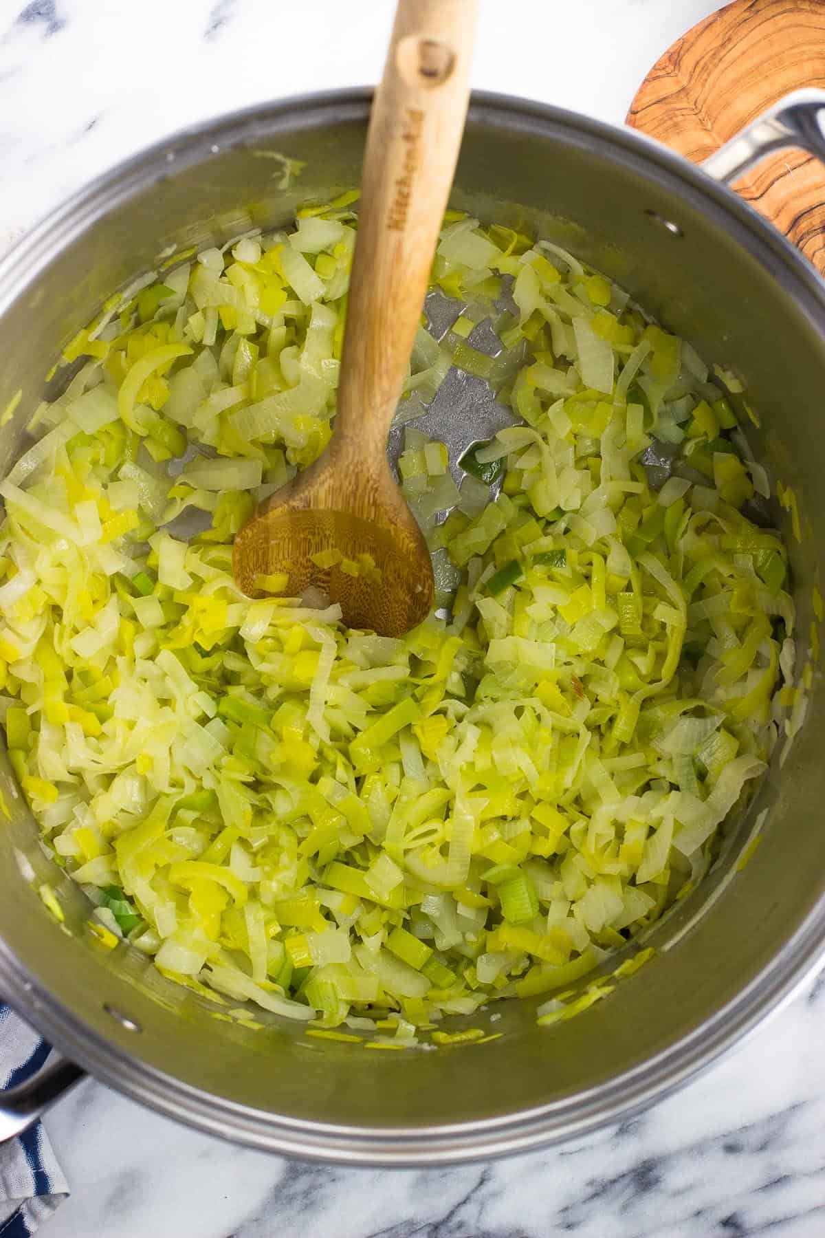 A wooden spoon in the pot of sauteed leeks and onions.