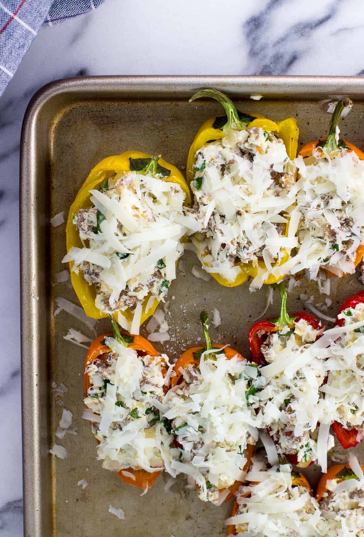 Shredded cheese on top of stuffed peppers on a sheet pan before baking.