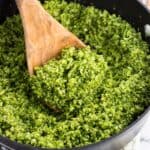 A pan of pesto broccoli rice with a wooden spoon scooping it.