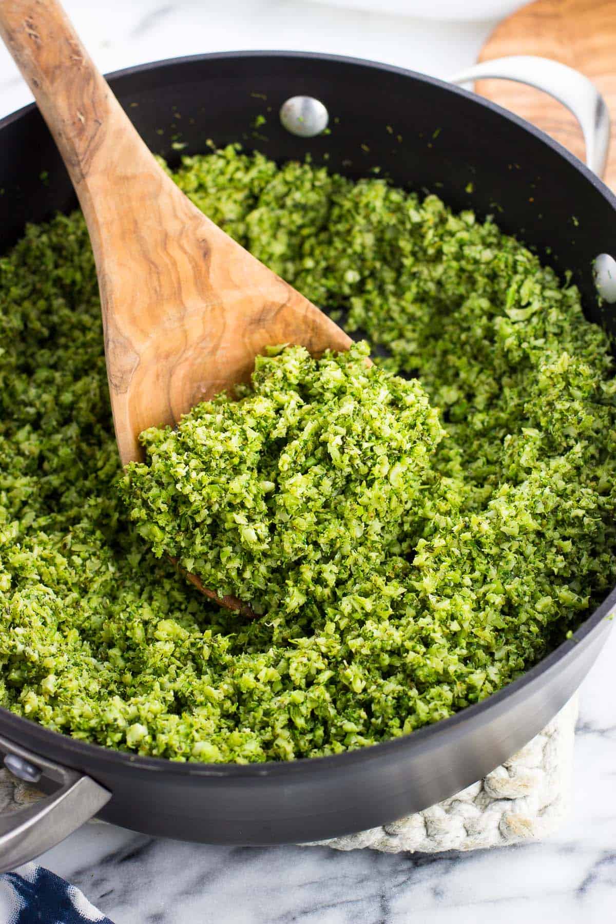 A pan of pesto broccoli rice with a wooden spoon scooping it.