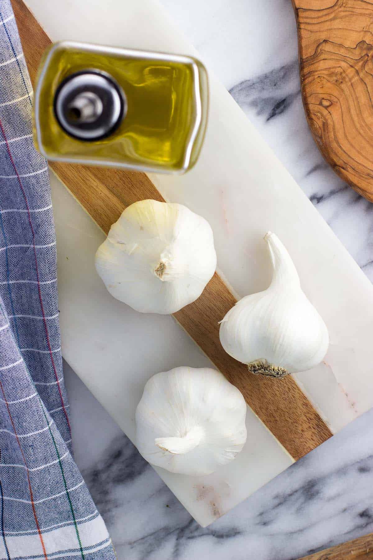 Three heads of garlic and an olive oil dispenser on a board.