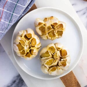 Three whole roasted garlic heads on a plate.