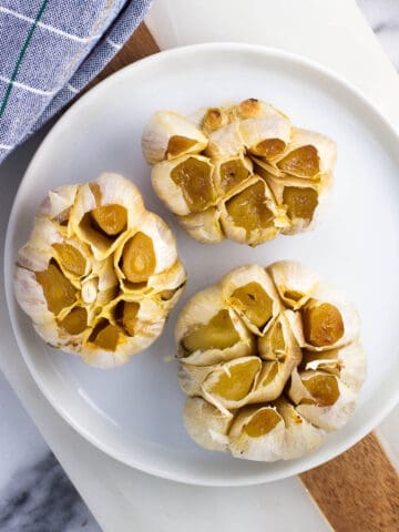 Three whole roasted garlic heads on a plate.