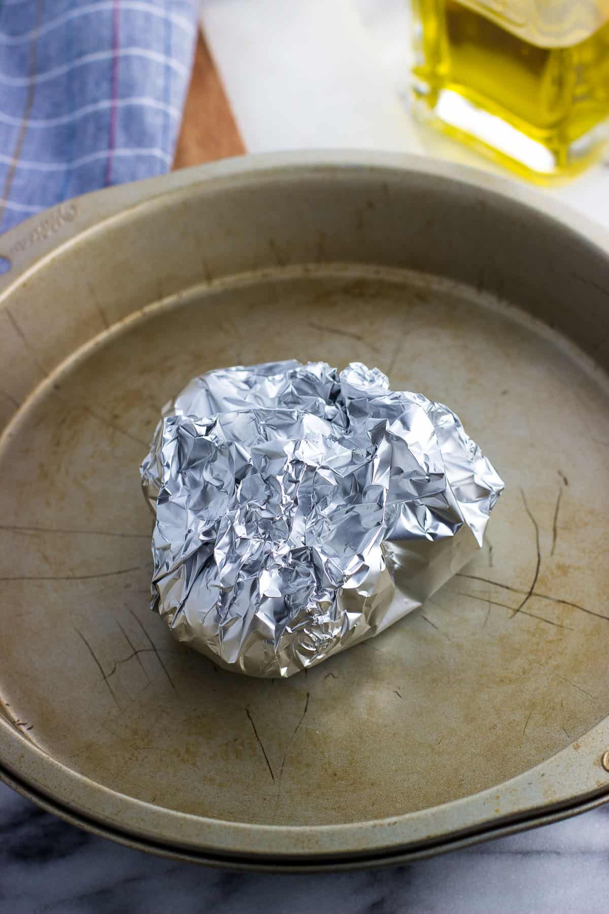 A foil-wrapped package of garlic heads on a pan.