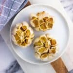 Three whole roasted garlic heads on a plate.