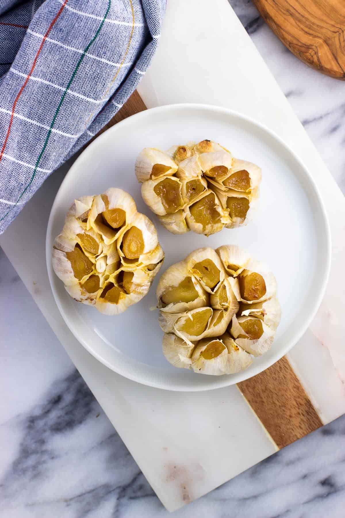 Three whole roasted garlic heads on a plate.