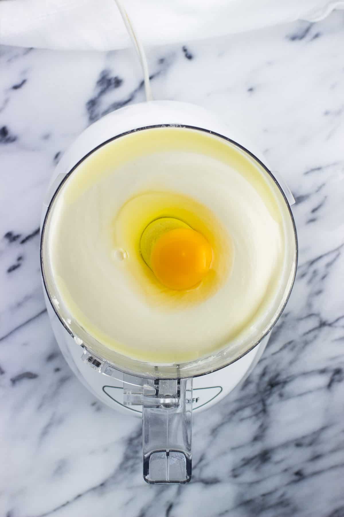 An egg added to the cream cheese/sugar mixture in the food processor.