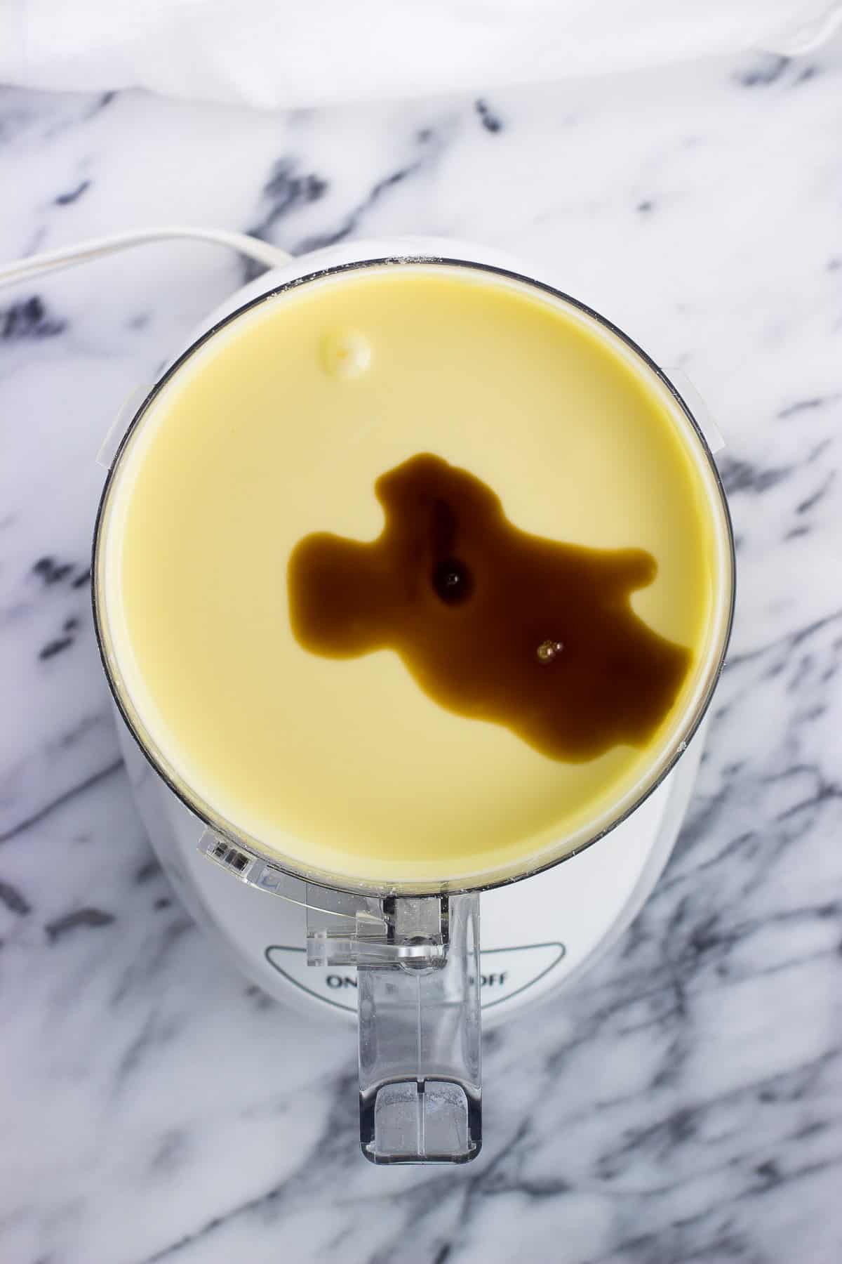 Vanilla extract poured into the cheesecake mixture in the food processor.