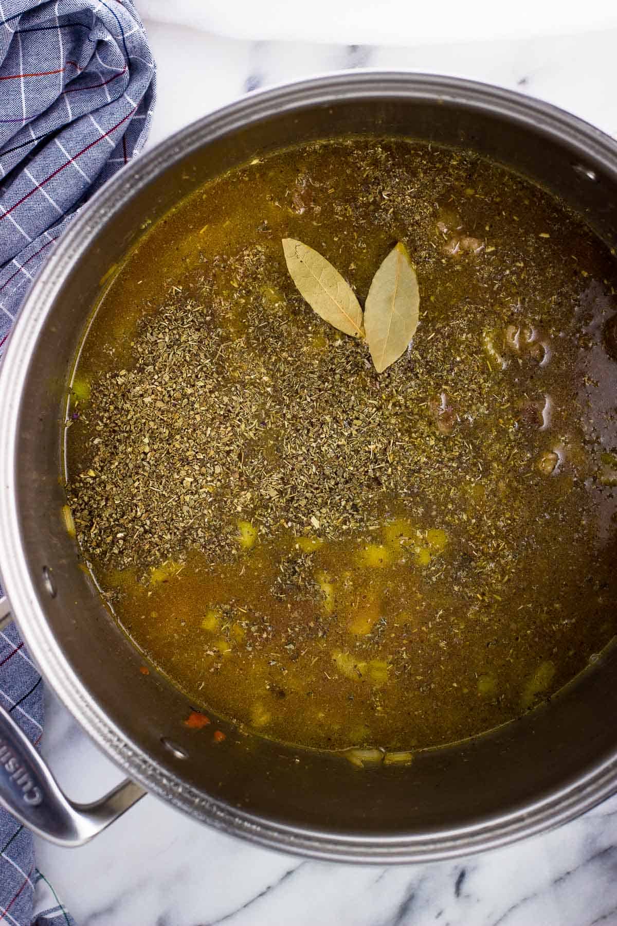 Dried spices, bay leaves, and broth added to the pot.