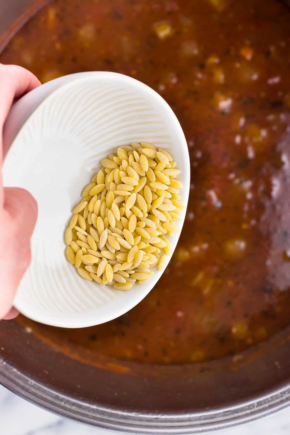 Orzo being poured into the bowl of soup.