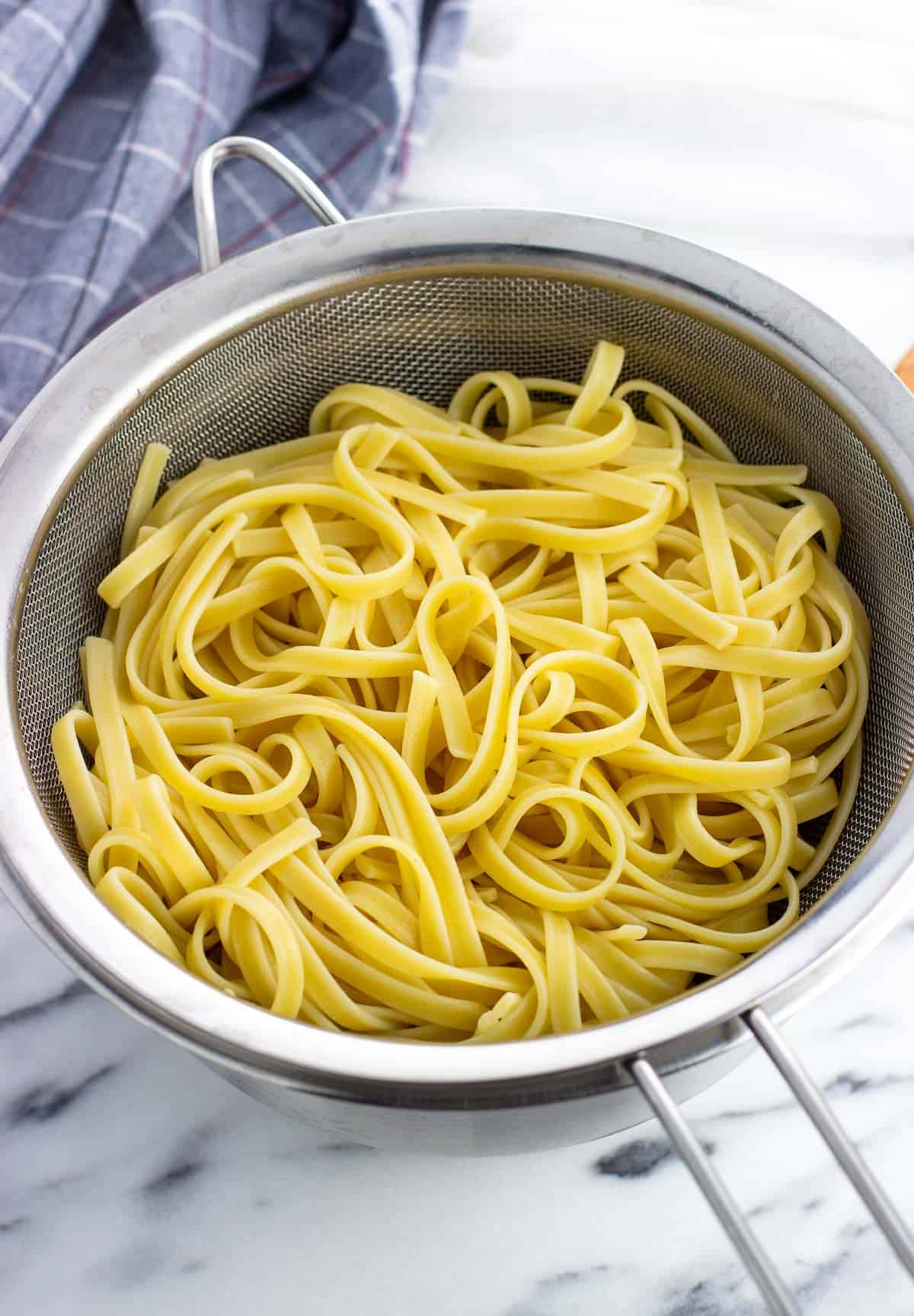 Cooked fettuccine in a large metal colander.