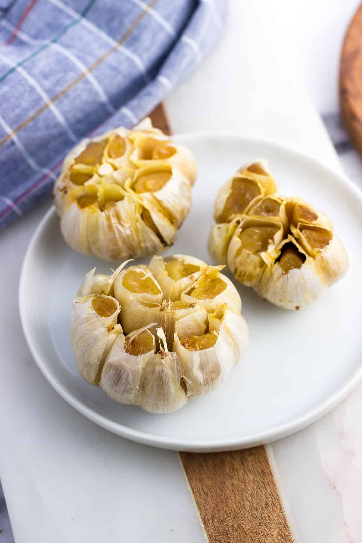 Three roasted garlic bulbs on a plate.