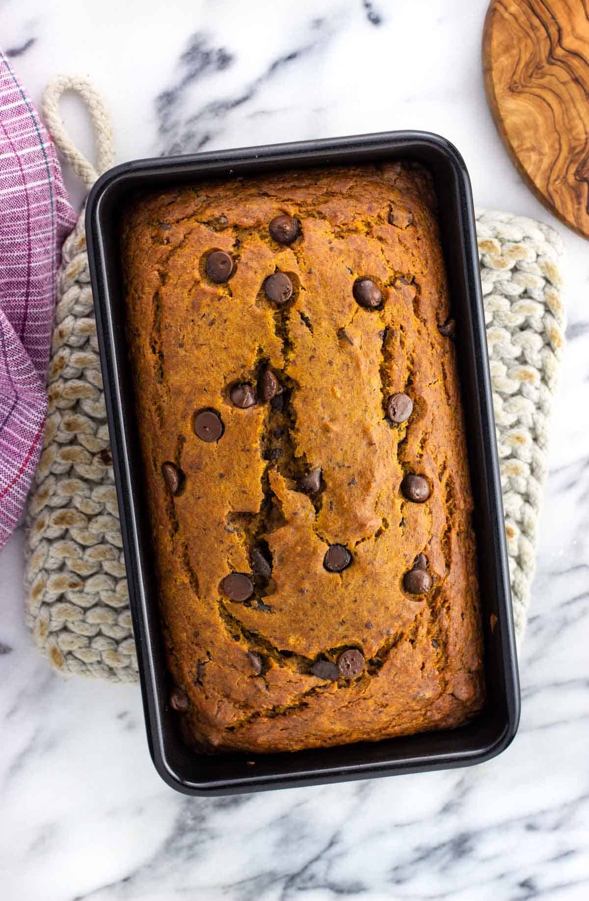 A loaf of pumpkin banana bread in a pan on a trivet.