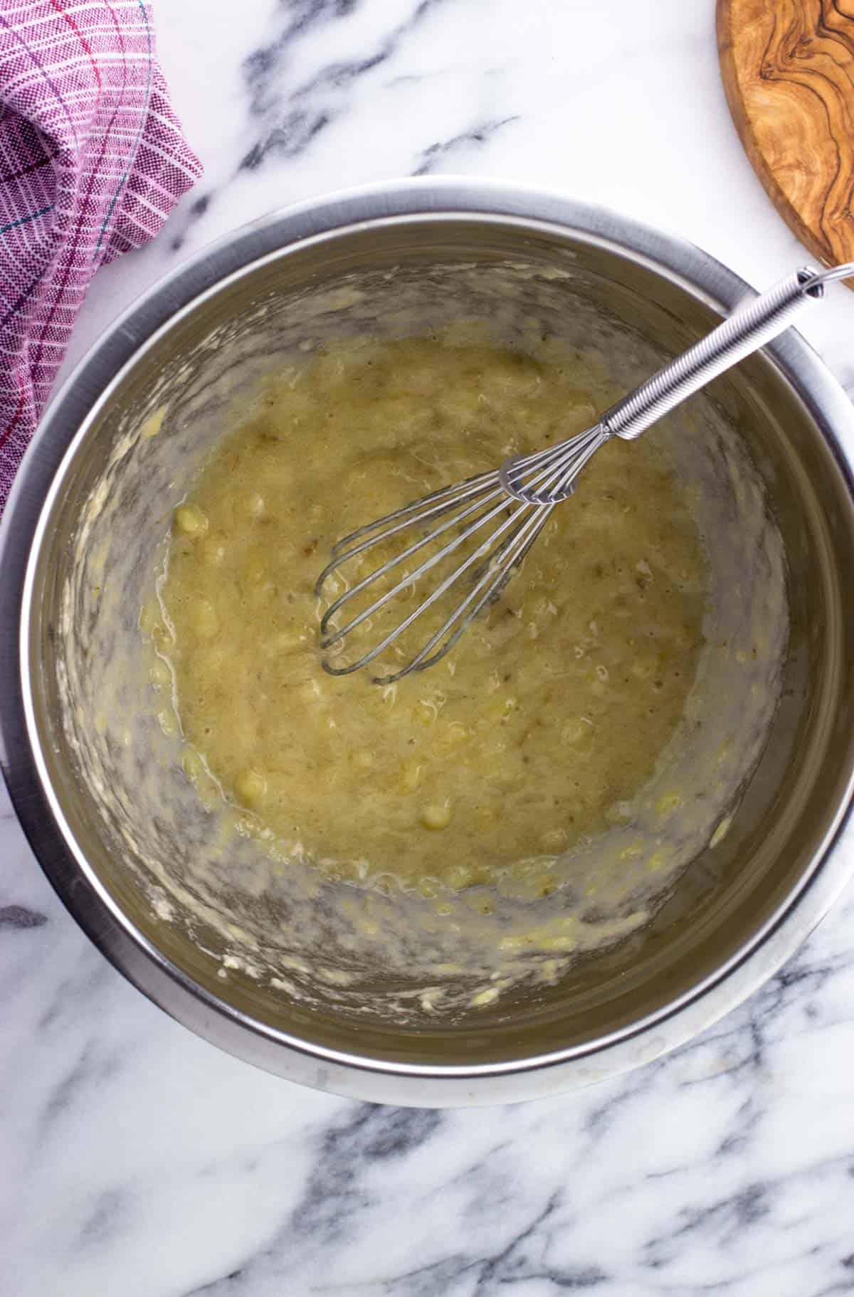 Mashed banana in a bowl with a whisk.