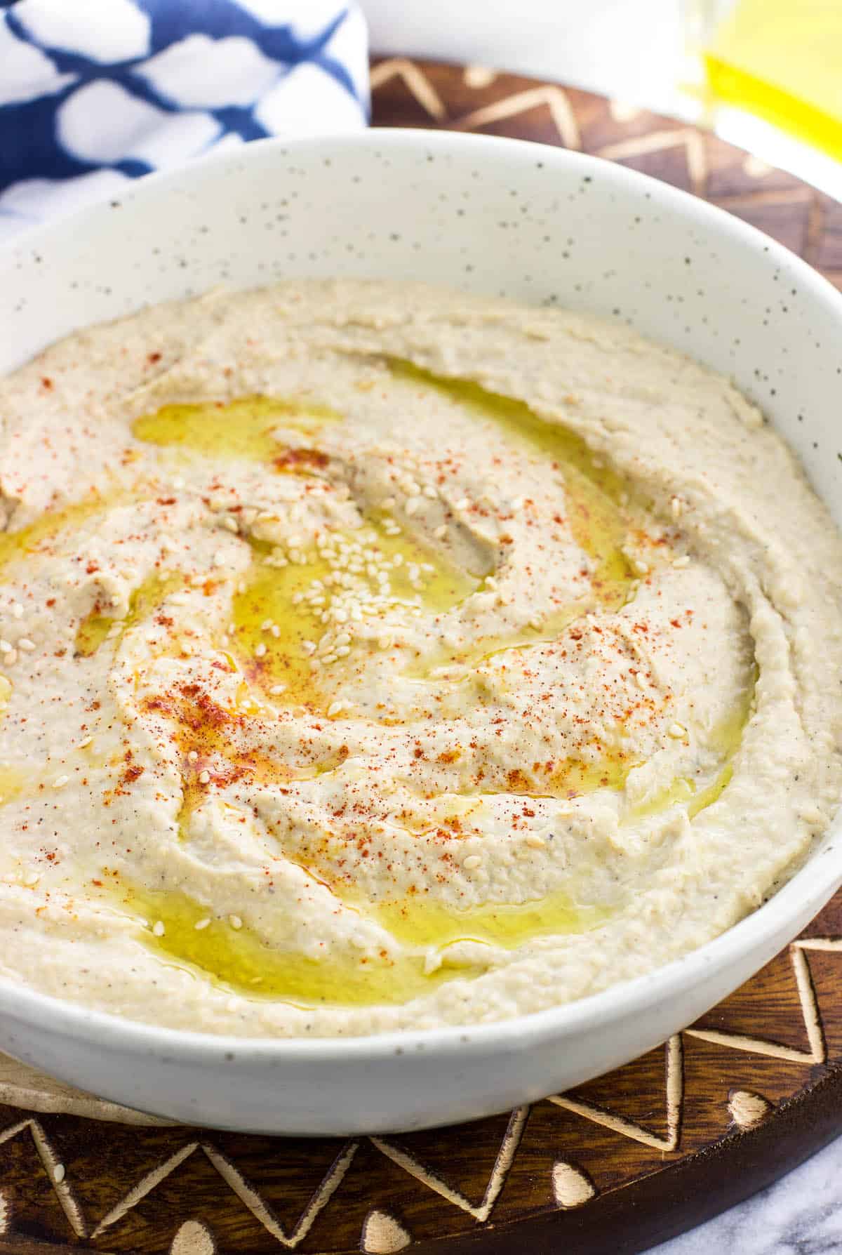 A serving bowl of hummus with olive oil, paprika, and sesame seeds.