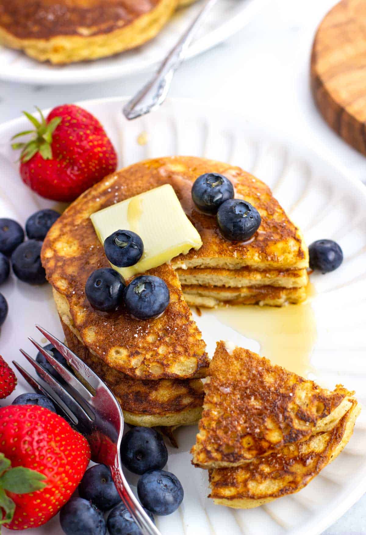 A stack of pancakes topped with a pat of butter with a wedge cut out.