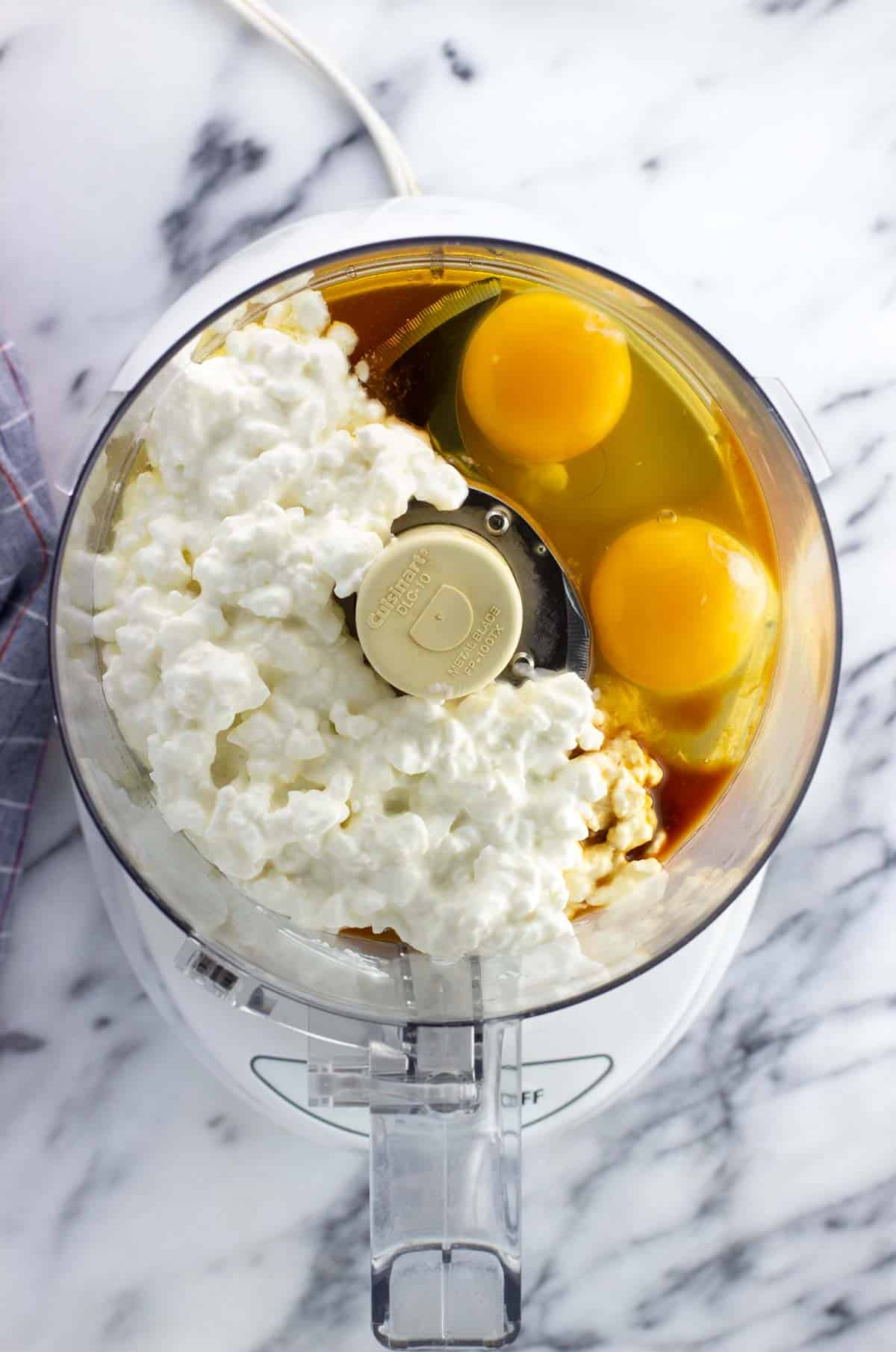 Cottage cheese, eggs, maple syrup, and vanilla extract added to the bowl of a food processor.