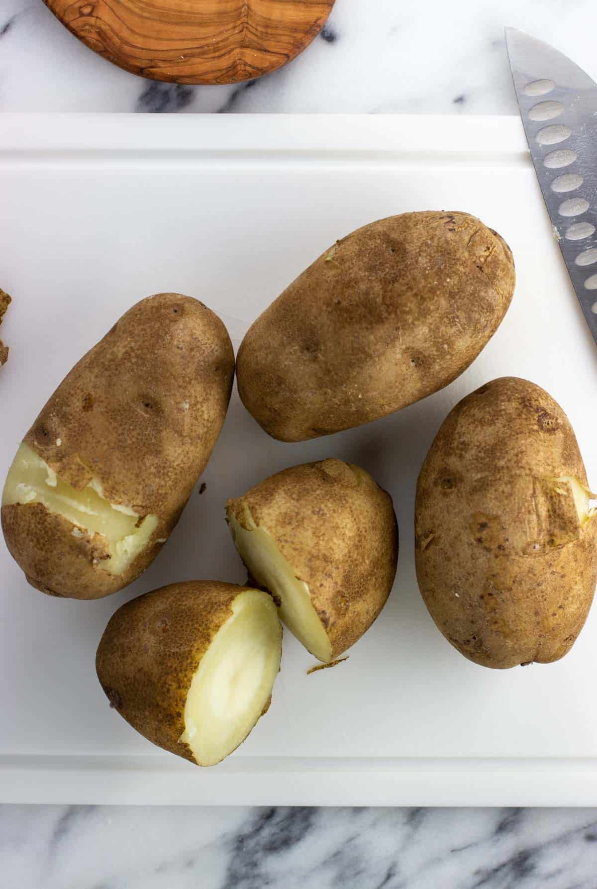 Four parboiled potatoes on a cutting board, with one sliced in half.
