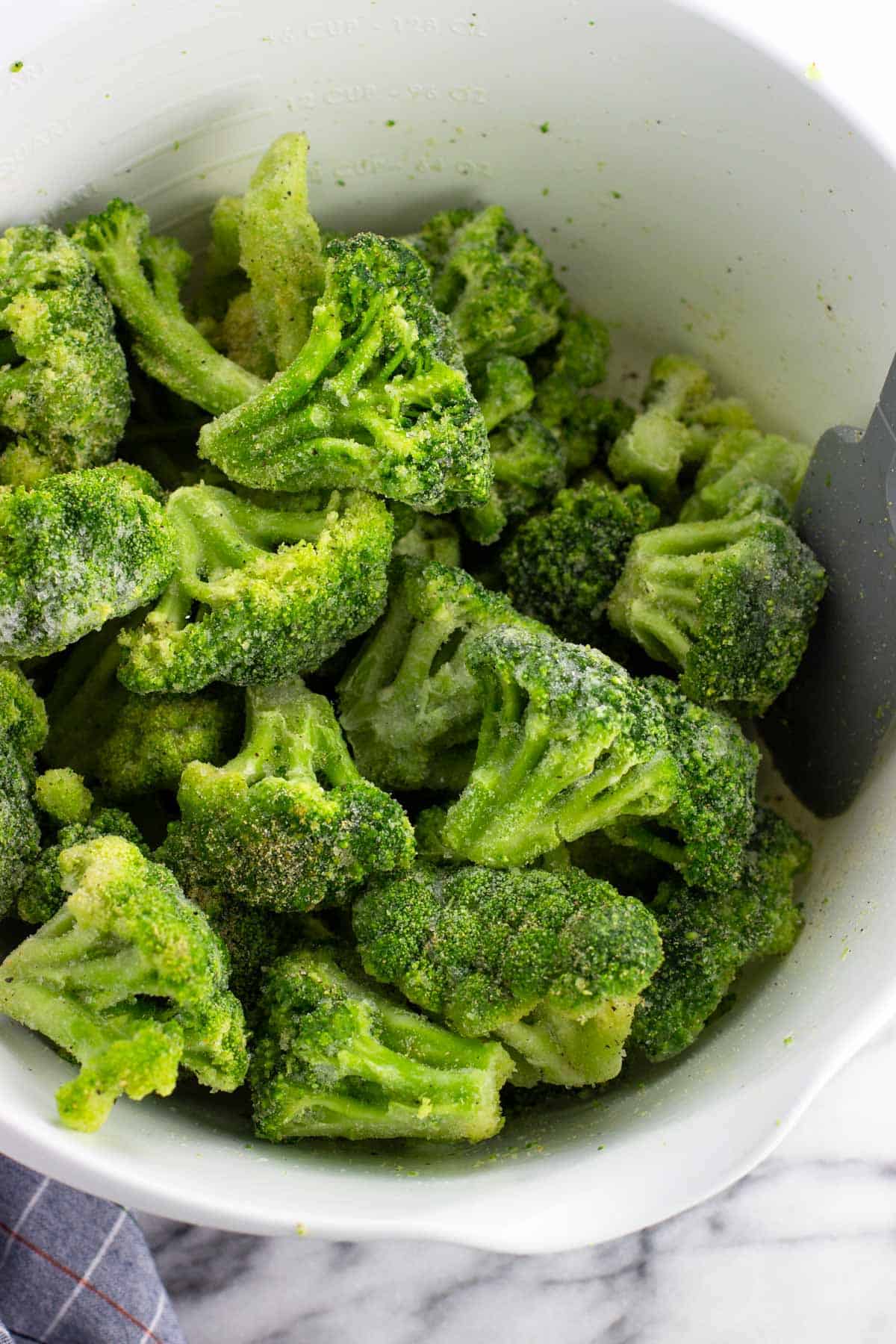 Frozen broccoli in a mixing bowl drizzled with oil and spices.