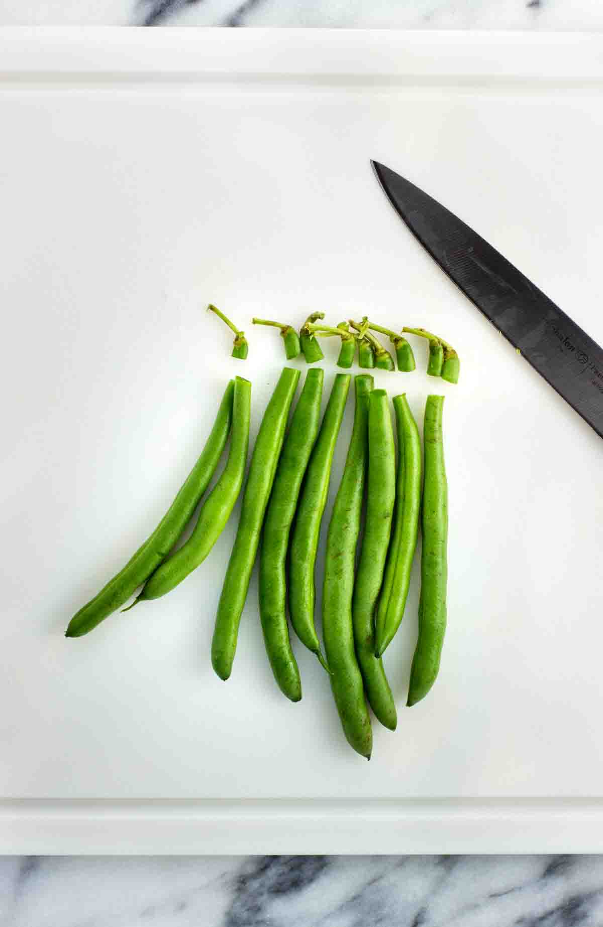 Green beans on a cutting board with the tops trimmed.