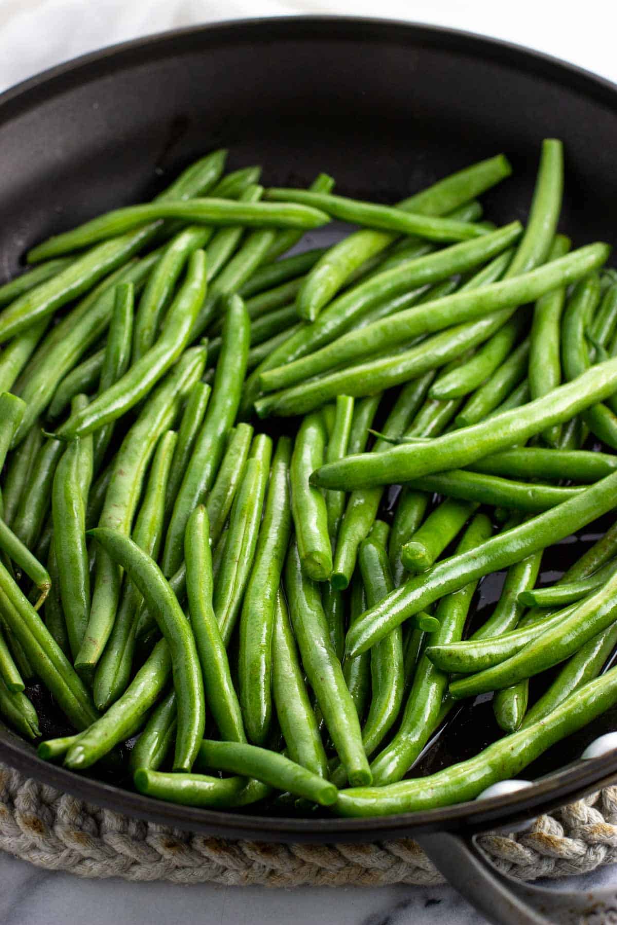 Green beans coated in olive oil in a pan.