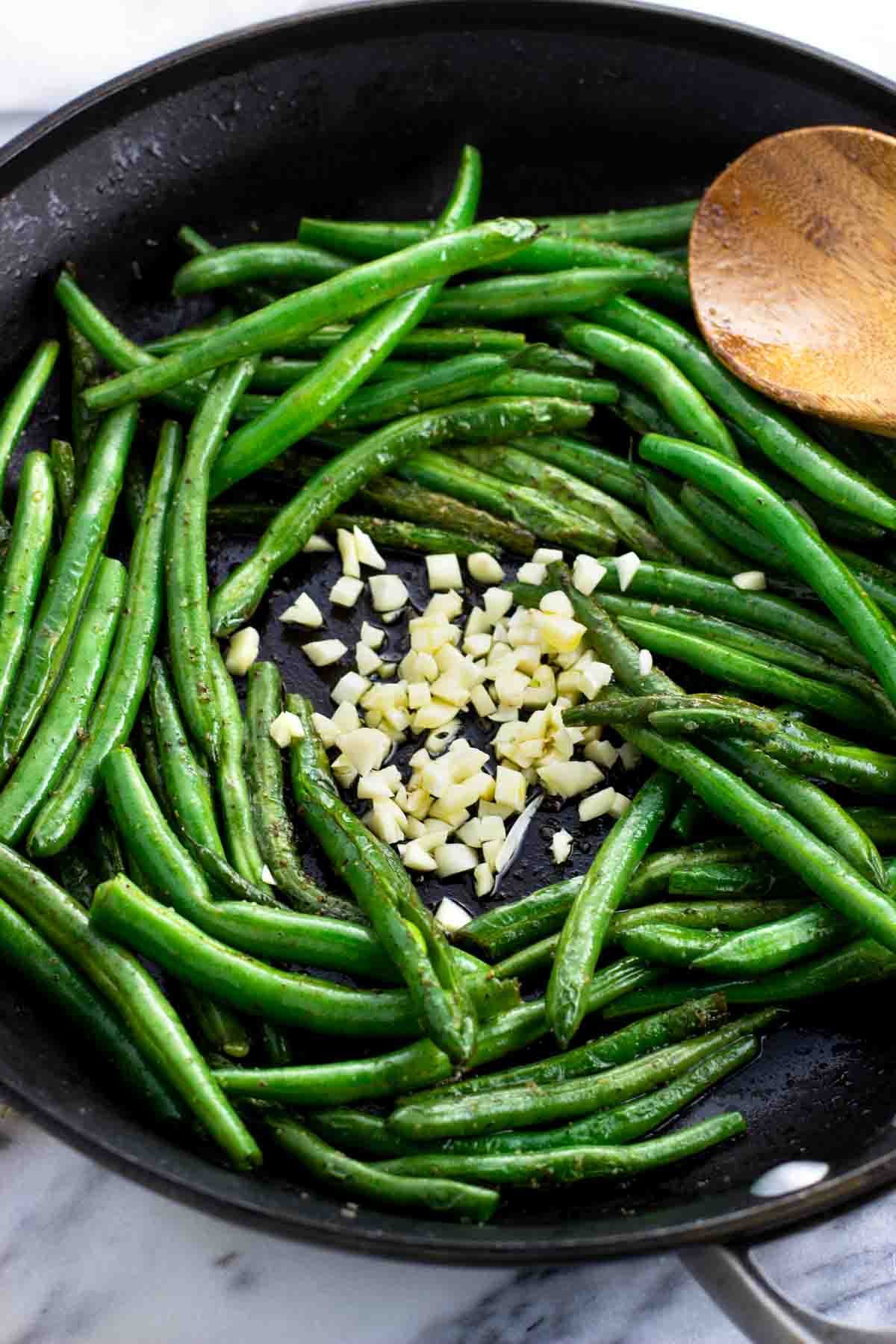 Chopped garlic surrounded by green beans in a pan.