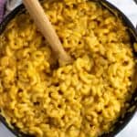 Pumpkin mac and cheese in a pan with a wooden spoon.