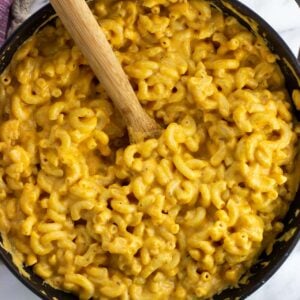 Pumpkin mac and cheese in a pan with a wooden spoon.
