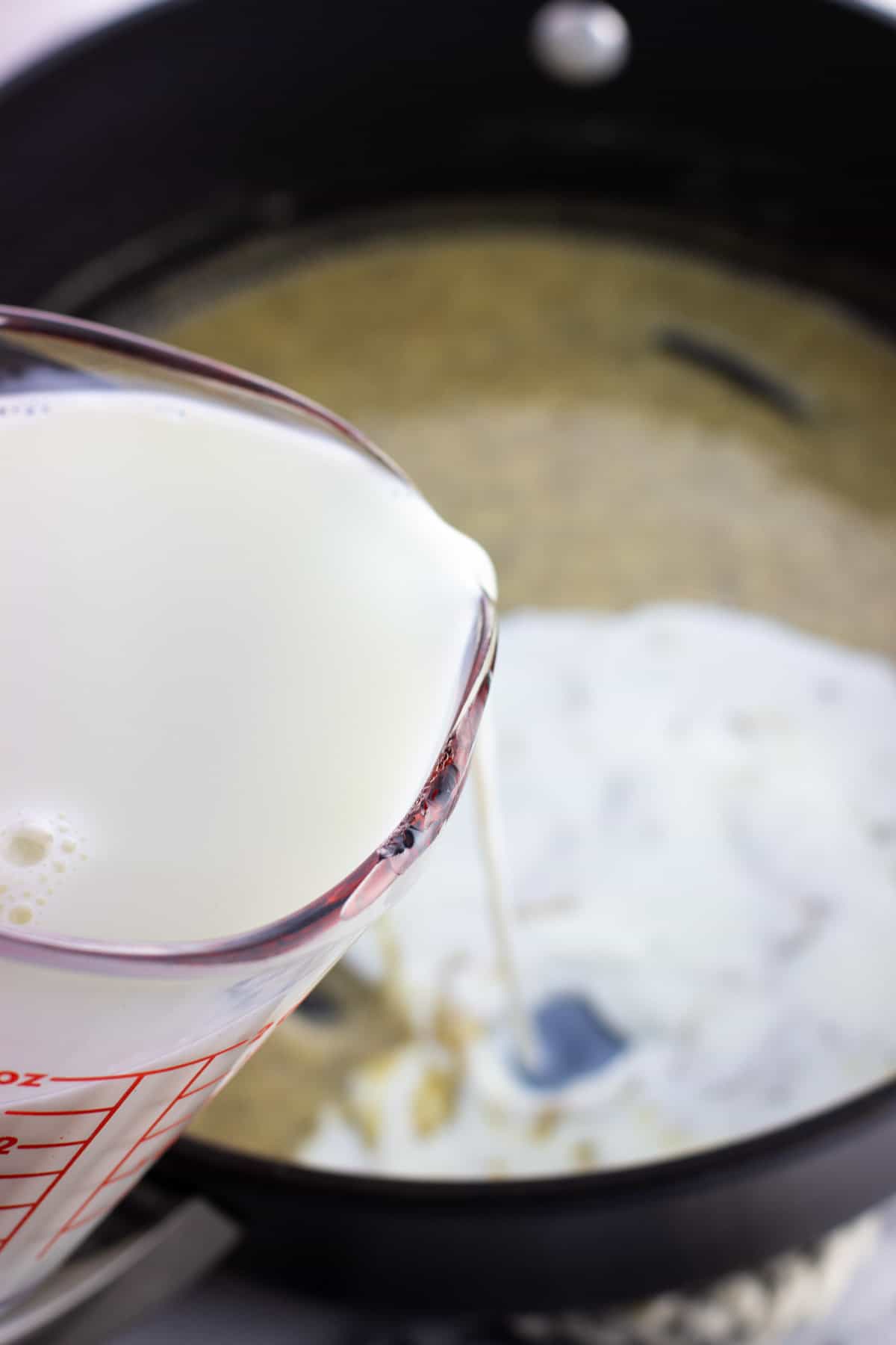 Milk being poured into the pan of roux.