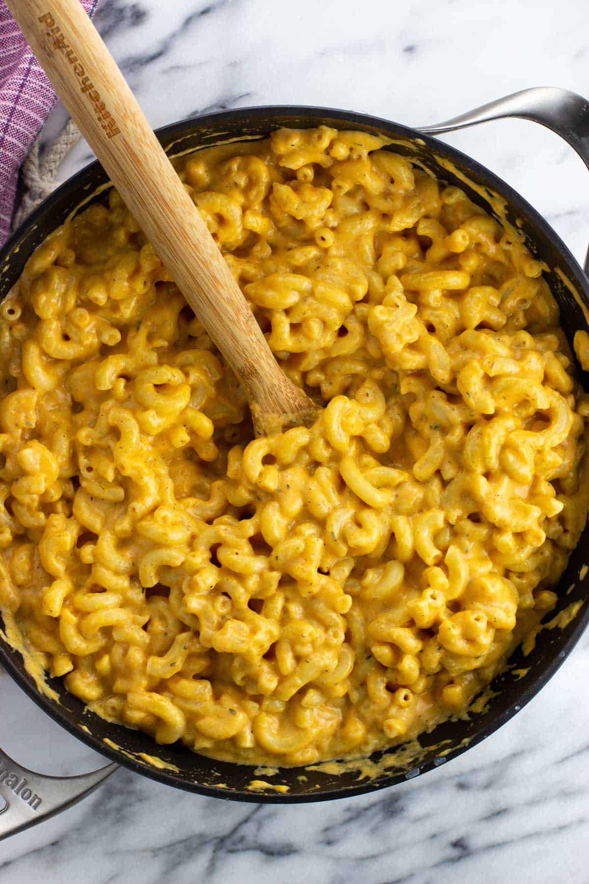 Pumpkin mac and cheese in a pan with a wooden spoon.