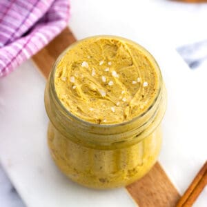 A glass jar of whipped pumpkin spice butter topped with flaky salt.