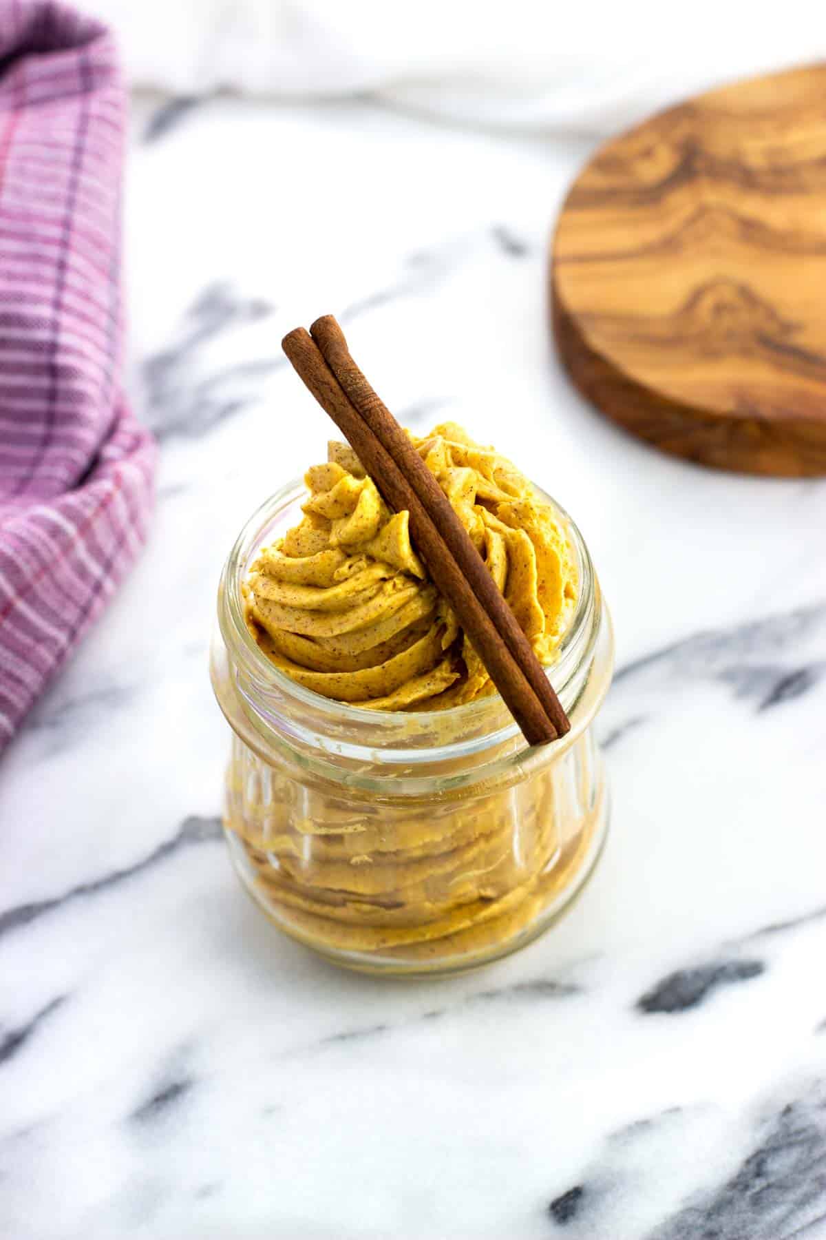 A jar of whipped pumpkin spice butter topped with a cinnamon stick.