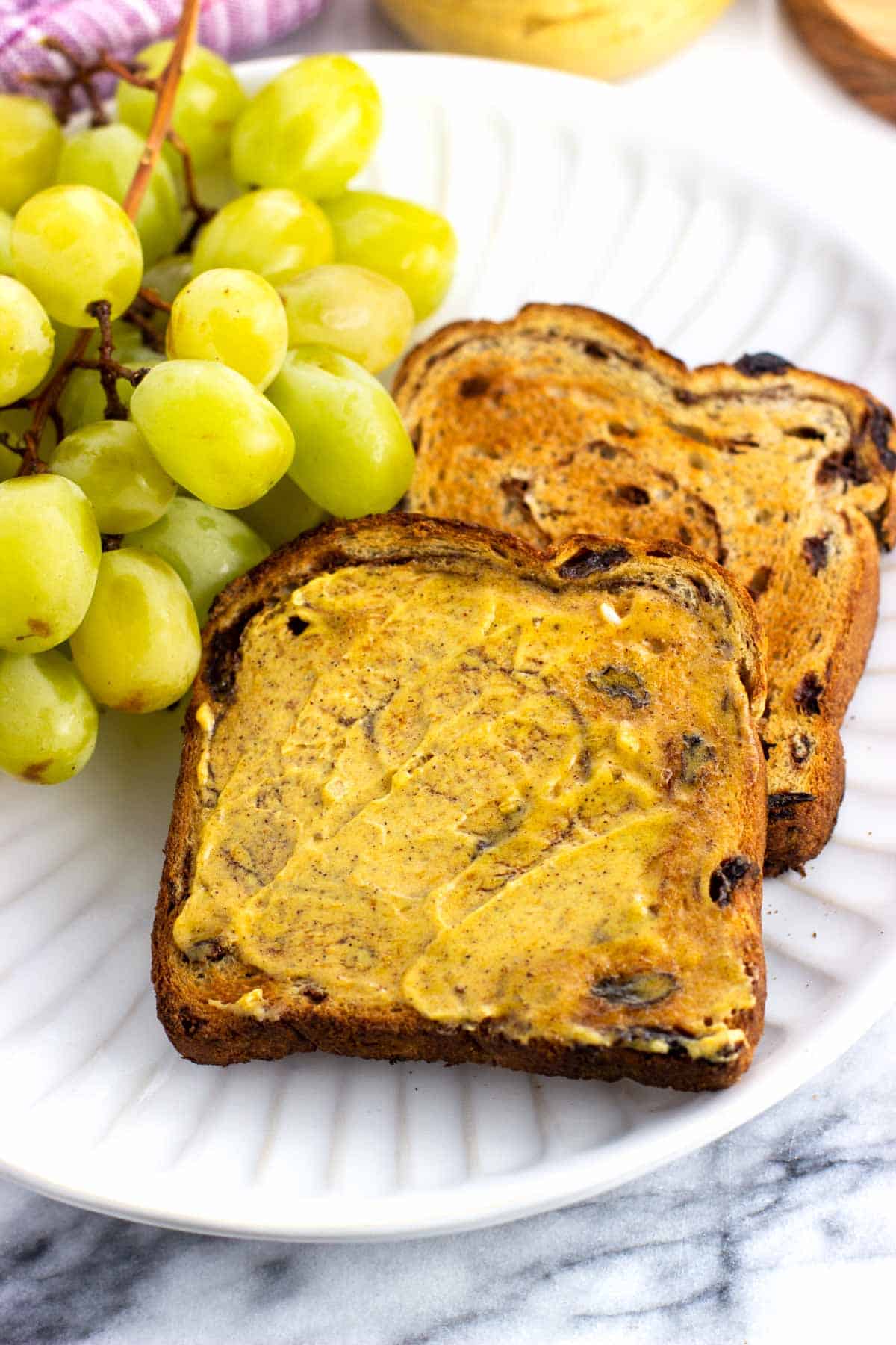 Toast slathered with pumpkin spice butter on a plate with grapes.