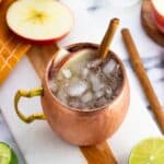 An apple cider mule garnished with apple slices and a cinnamon stick.