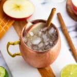 An apple cider mule garnished with apple slices and a cinnamon stick.