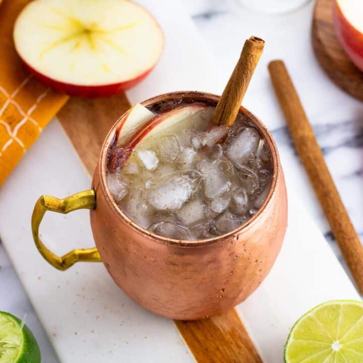 An apple cider mule garnished with apple slices and a cinnamon stick.