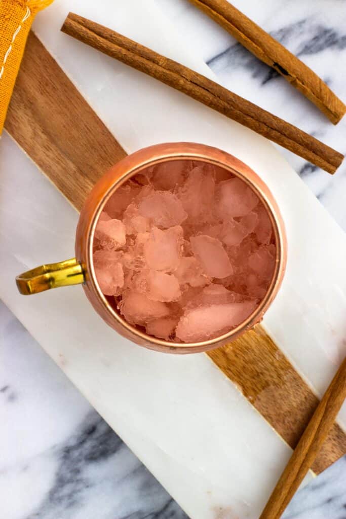 Crushed ice in a moscow mule cup surrounded by cinnamon sticks.