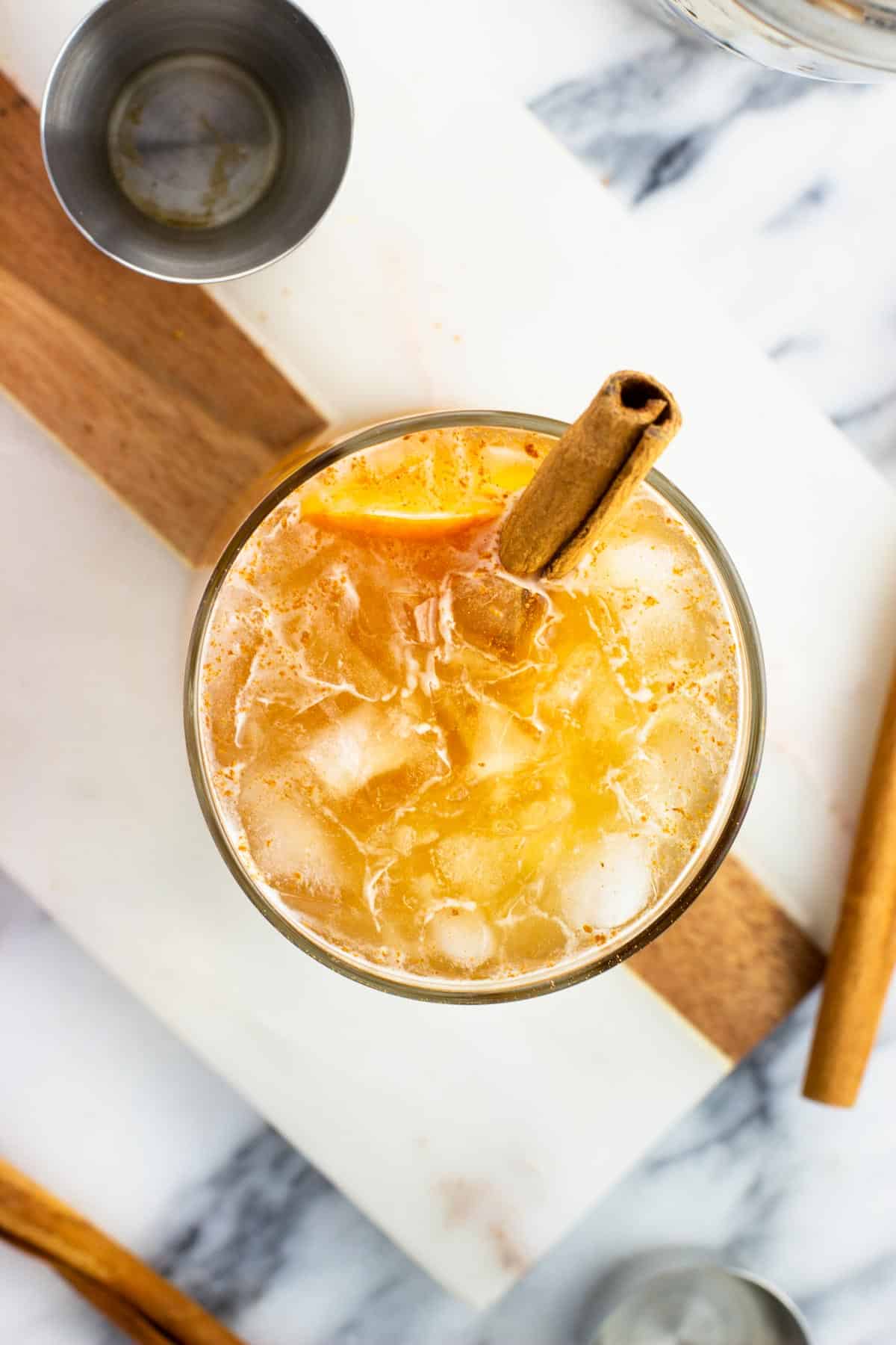 A top view of a cinnamon stick and orange peel in a cocktail.