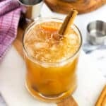 A bourbon apple cider cocktail garnished with orange peel and a cinnamon stick.