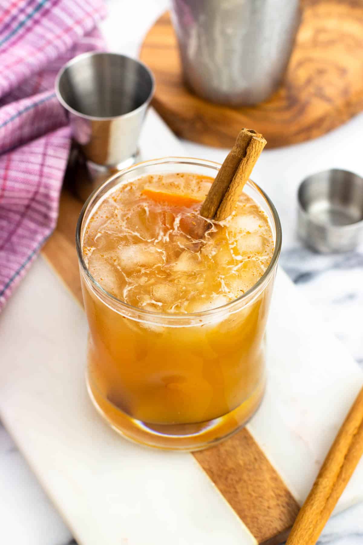 A bourbon apple cider cocktail garnished with orange peel and a cinnamon stick.