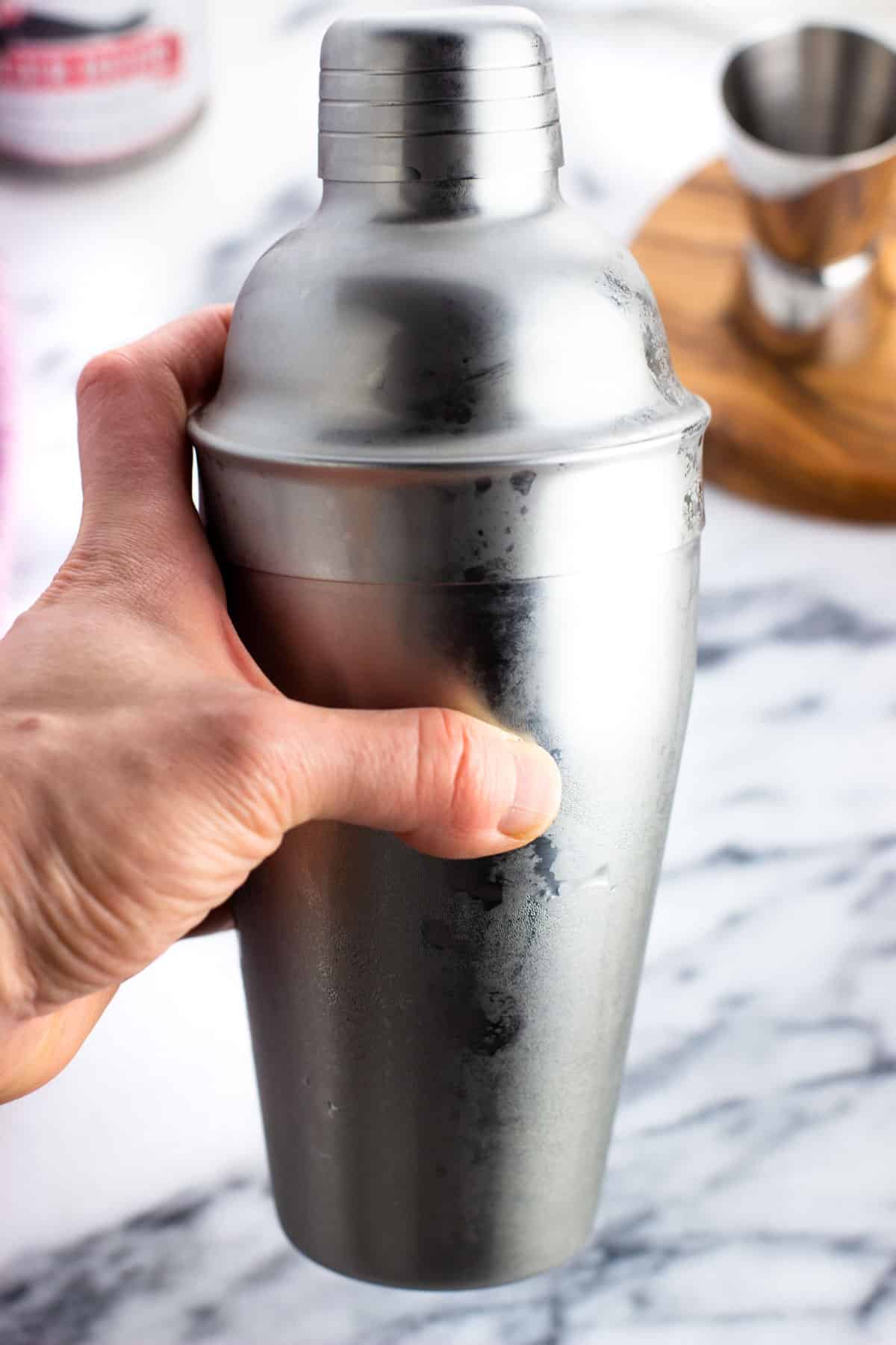 A hand holding a frosty metal cocktail shaker.
