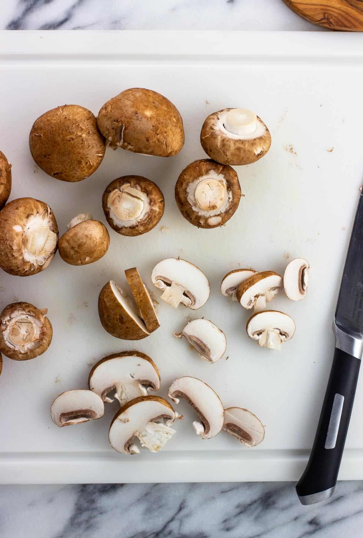 Mushrooms on a cutting board with some sliced.