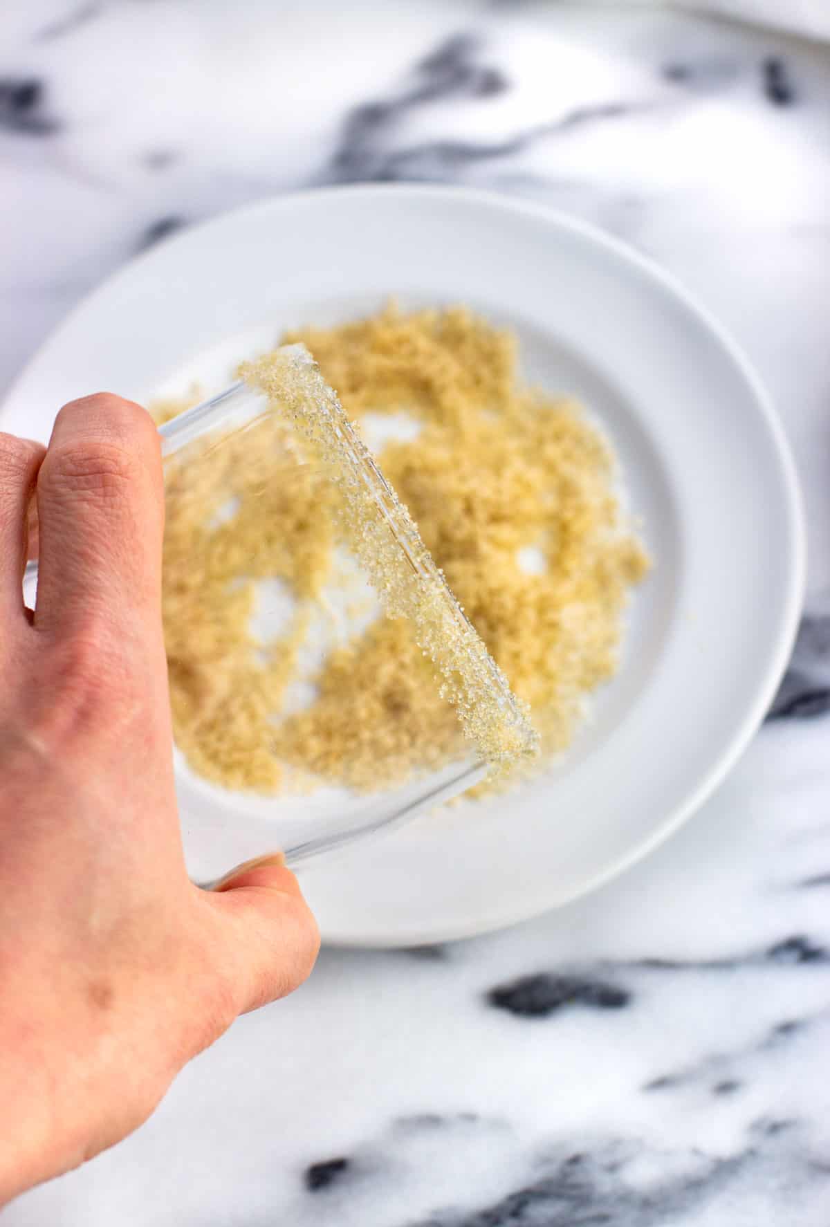 A hand dipping the rim of a glass into the sugar mixture.