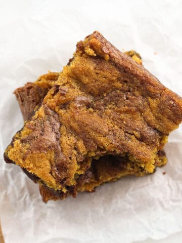 Two pumpkin brownies stacked on top of one another with a bite taken out of the top one.