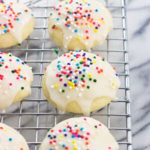 Glazed ricotta cookies with nonpareils on a wire rack.