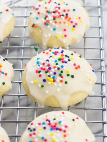 Glazed ricotta cookies with nonpareils on a wire rack.